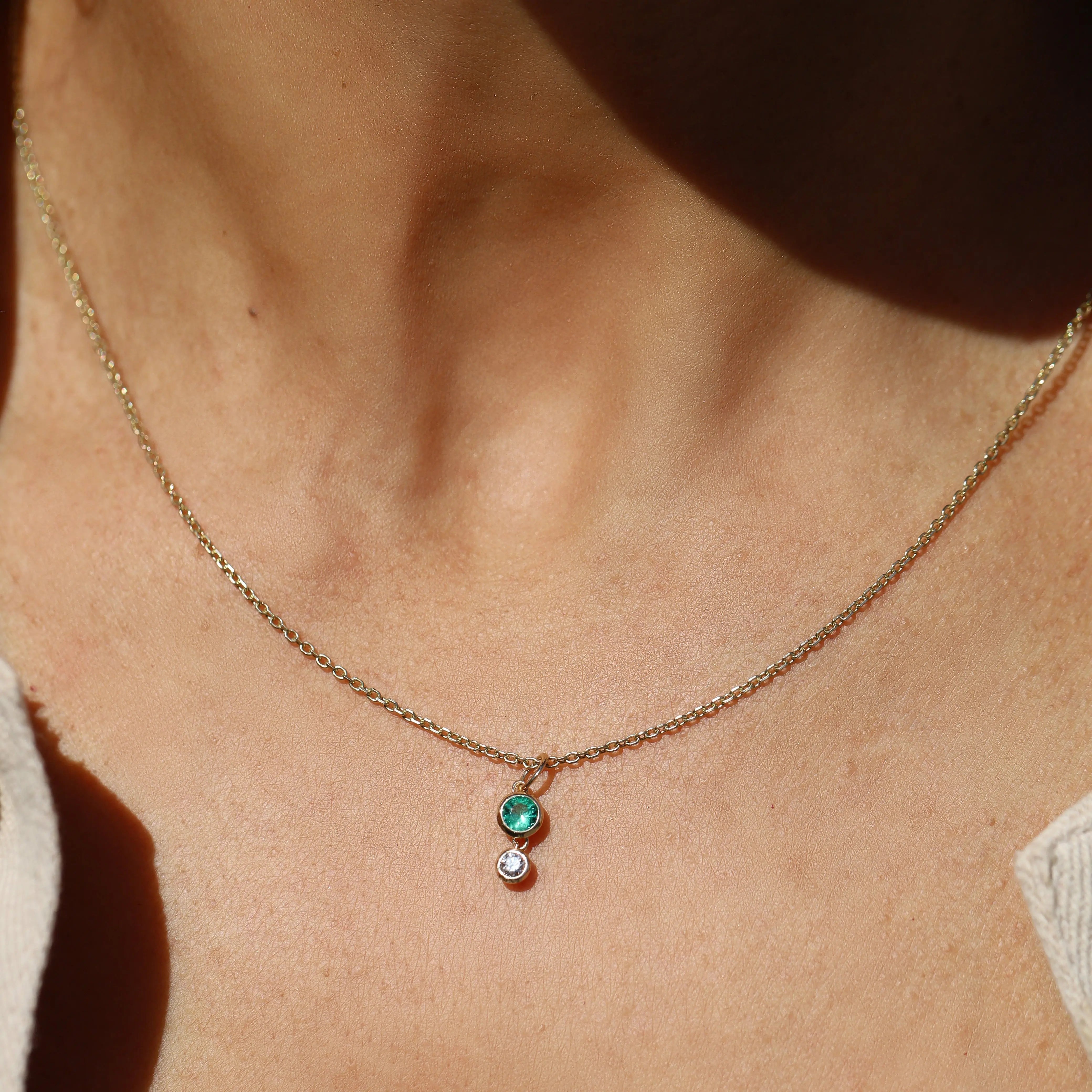 Necklace with a pendant featuring a green gemstone and small white gemstone on a person's neck.