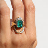 Gold ring with a green gemstone on a person's finger against a white background