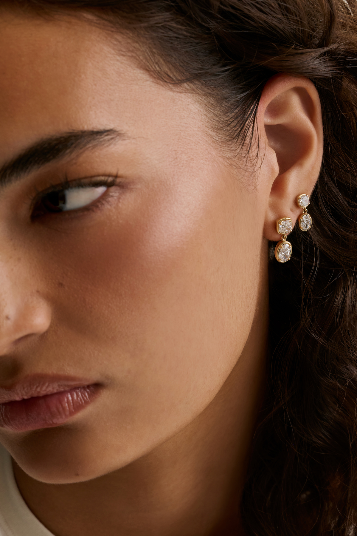 A close-up of a model's ear wearing a three-stone gold and diamond drop earring with diamonds.