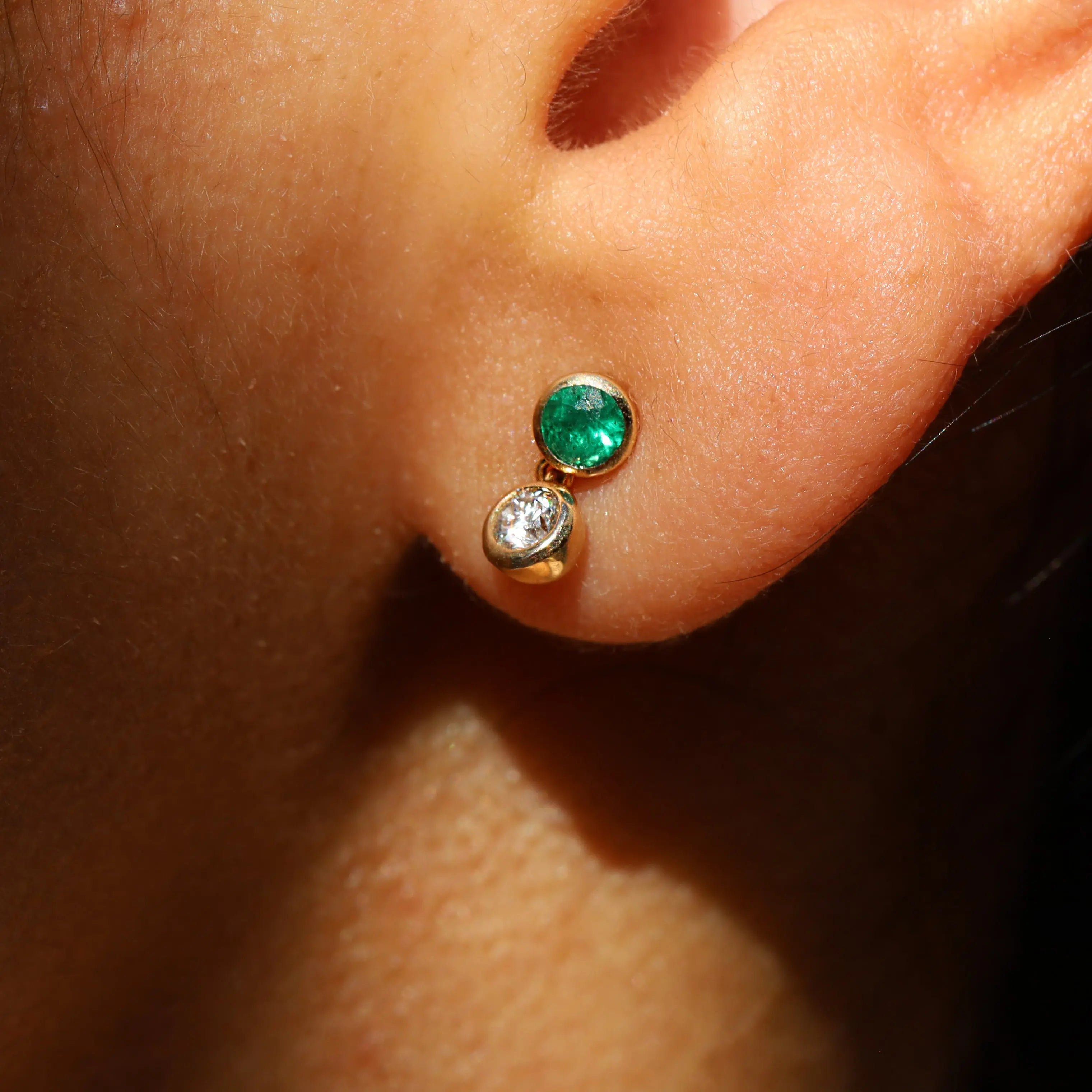 Gold earring with green gemstone worn on an ear
