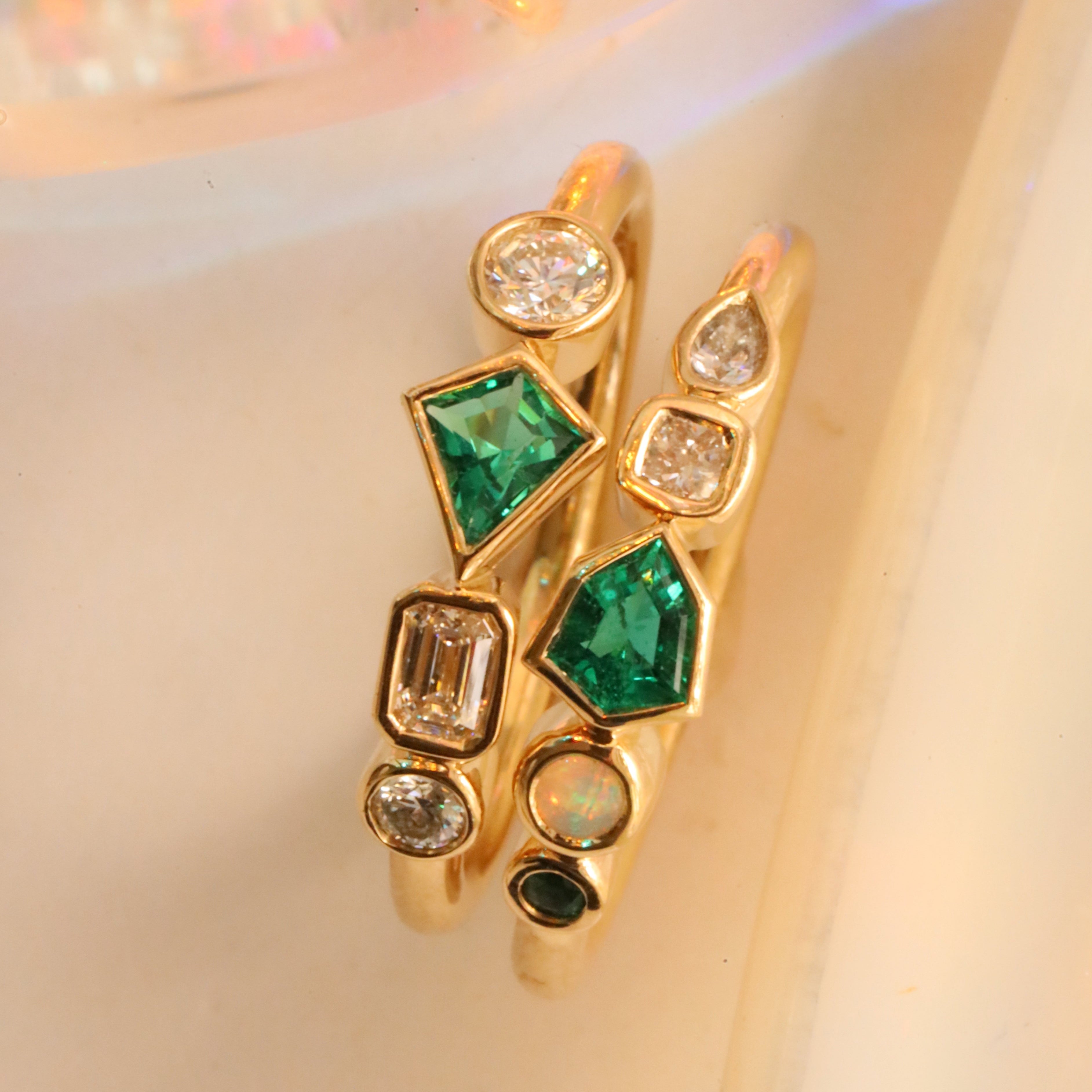 Flat lay of 0.13ct Emerald and Diamond Kaleidoscope Ring and 0.17ct Emerald, Opal and Diamond Kaleidoscope Ring