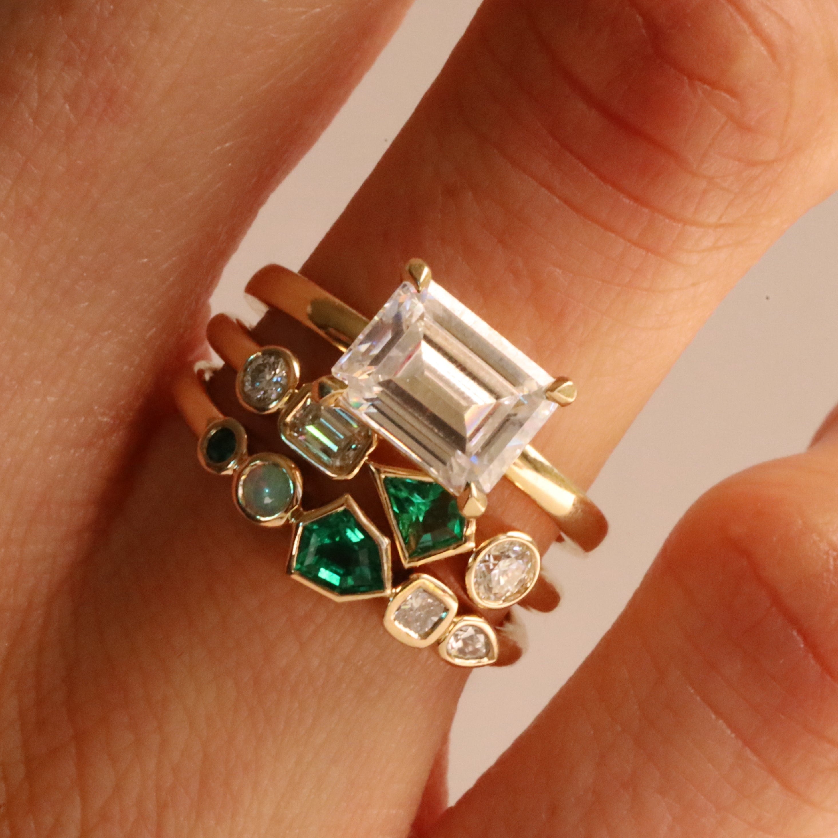 Close up of 0.13ct Emerald and Diamond Kaleidoscope Ring and 0.17ct Emerald, Opal and Diamond Kaleidoscope Ring stacked on woman's hand
