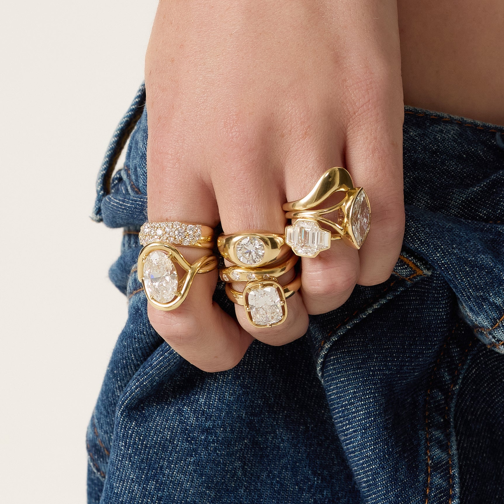 Hand wearing multiple gold rings with diamond accents against a denim background