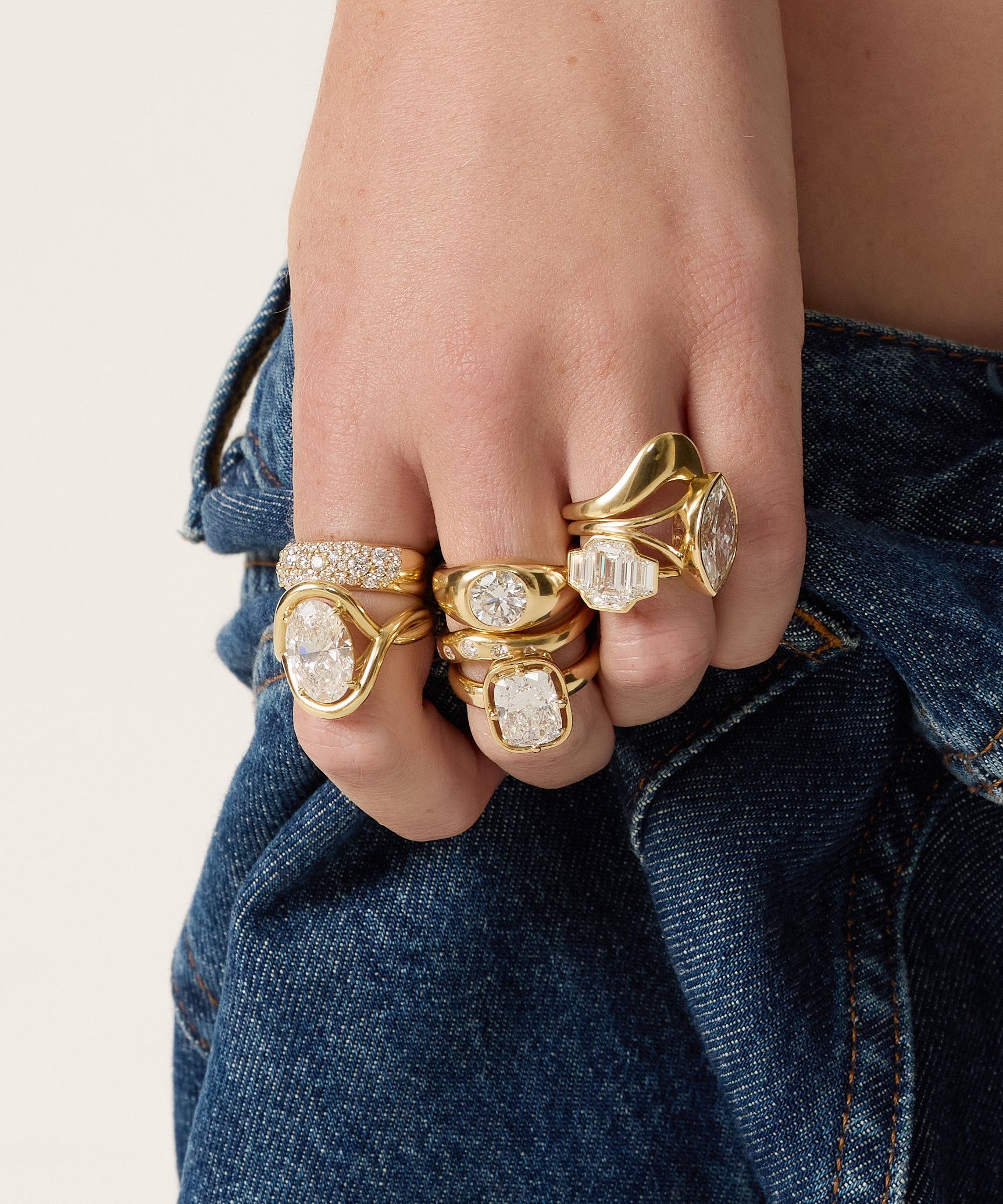 Hand wearing multiple gold rings with diamond accents against a denim background