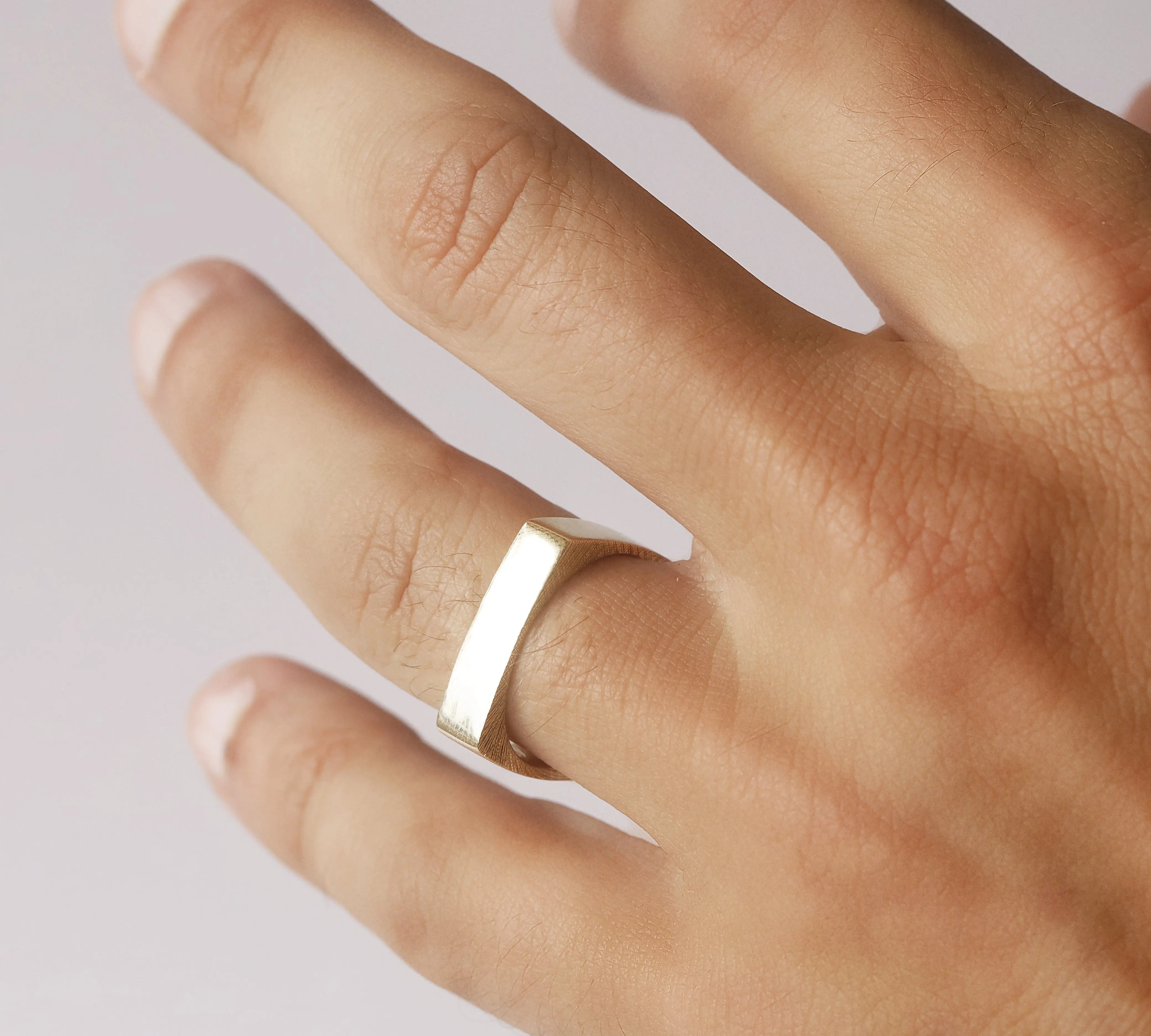 Hand wearing a gold ring on a light background