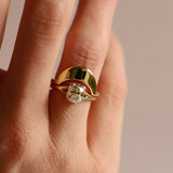 Gold ring with a diamond on a finger against a neutral background