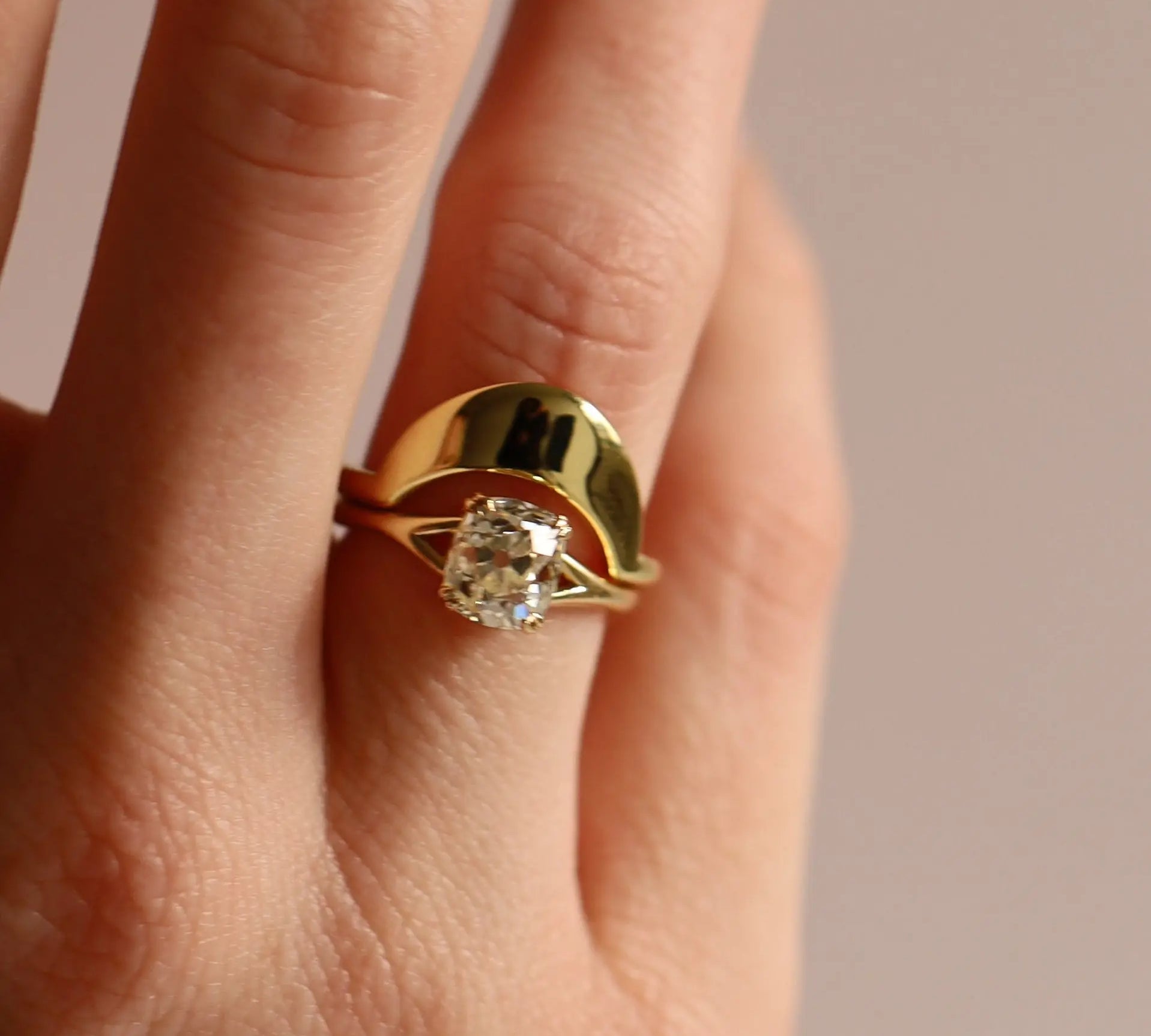 Gold ring with a diamond on a finger against a neutral background