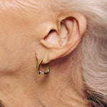 Close-up of an ear wearing a gold hoop earring with a neutral background