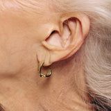 Close-up of an ear wearing a gold hoop earring with a neutral background