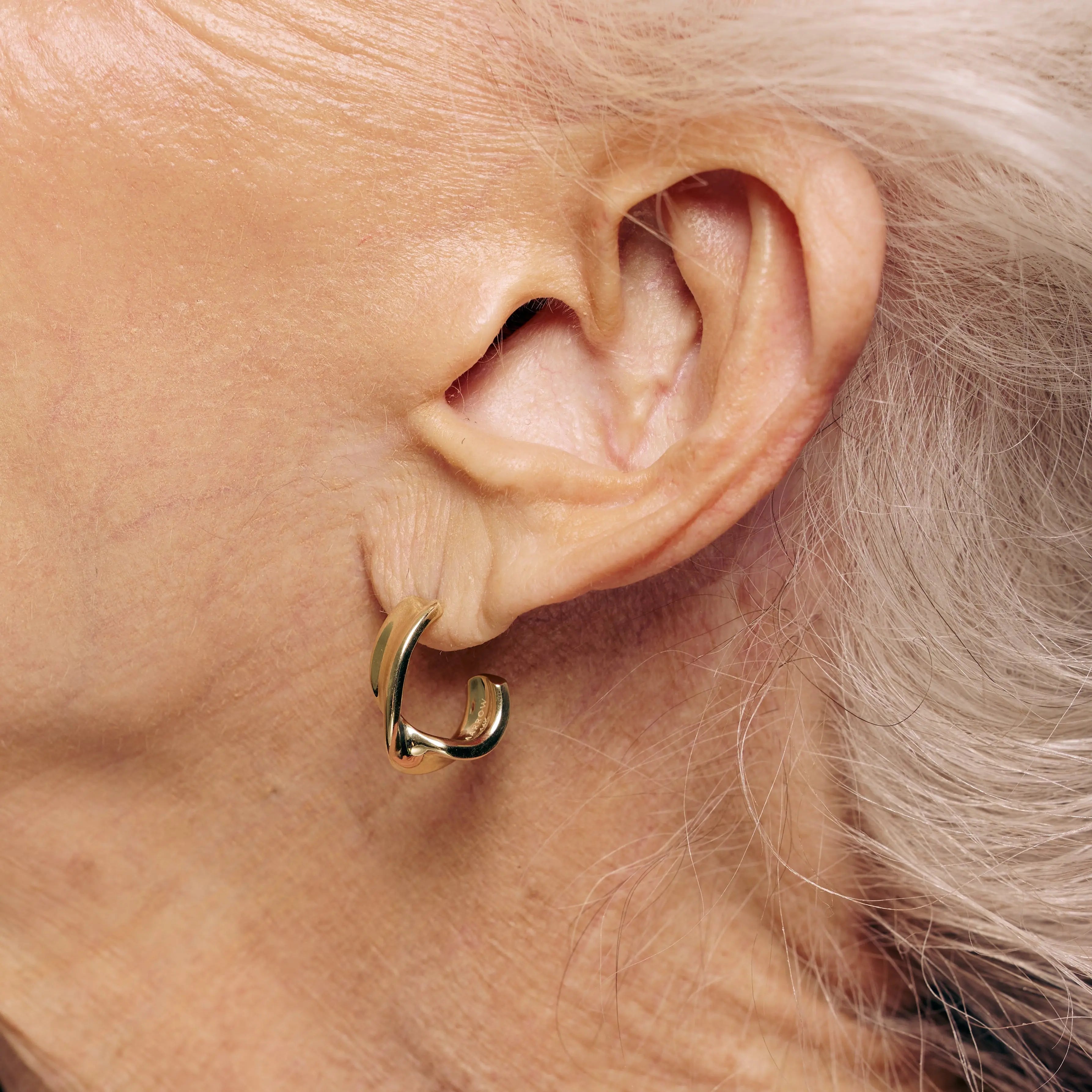 Close-up of an ear wearing a gold hoop earring with a neutral background