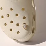 Beige clog shoe with a diamond charm on a light background