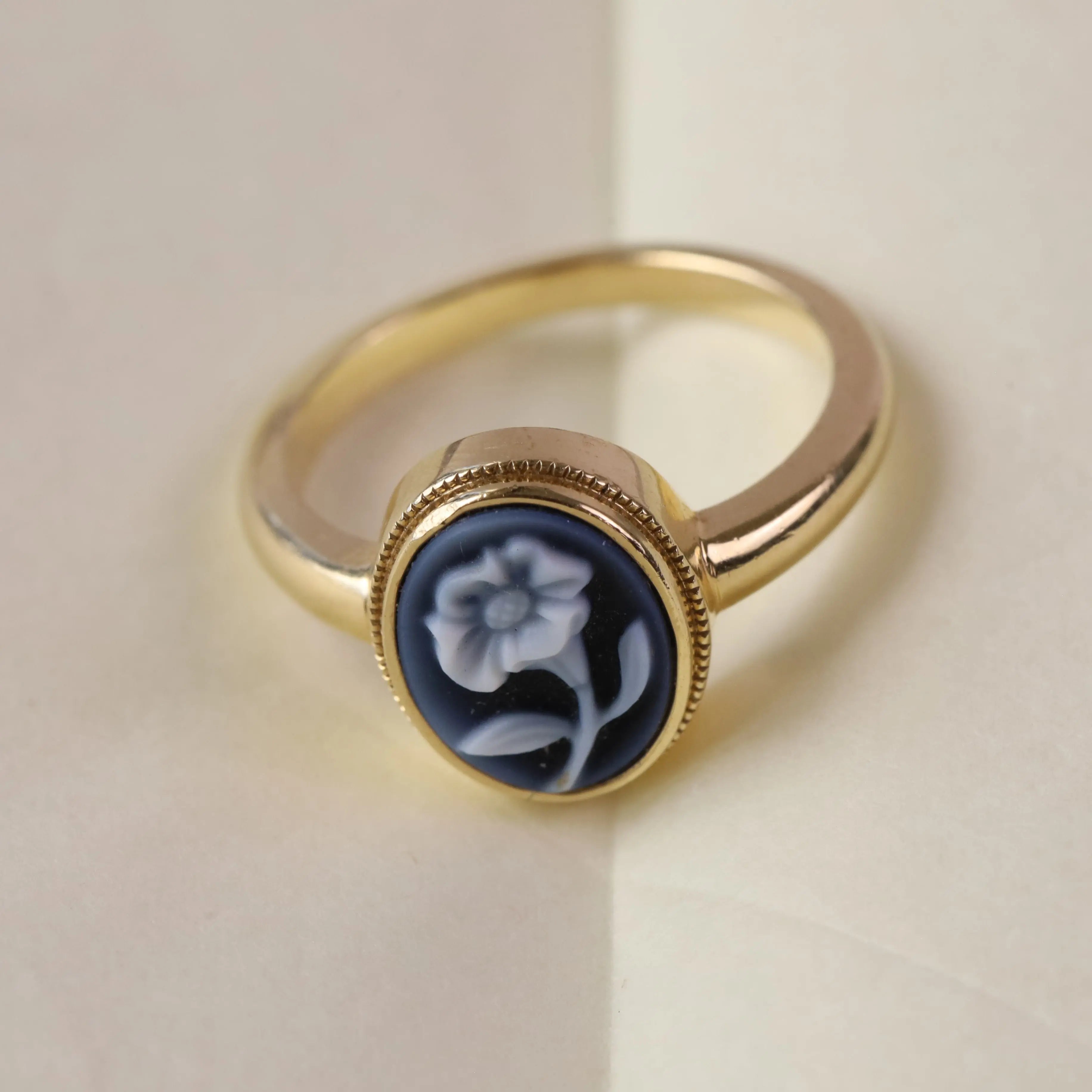 Gold ring with blue flower carving against a white backgound.