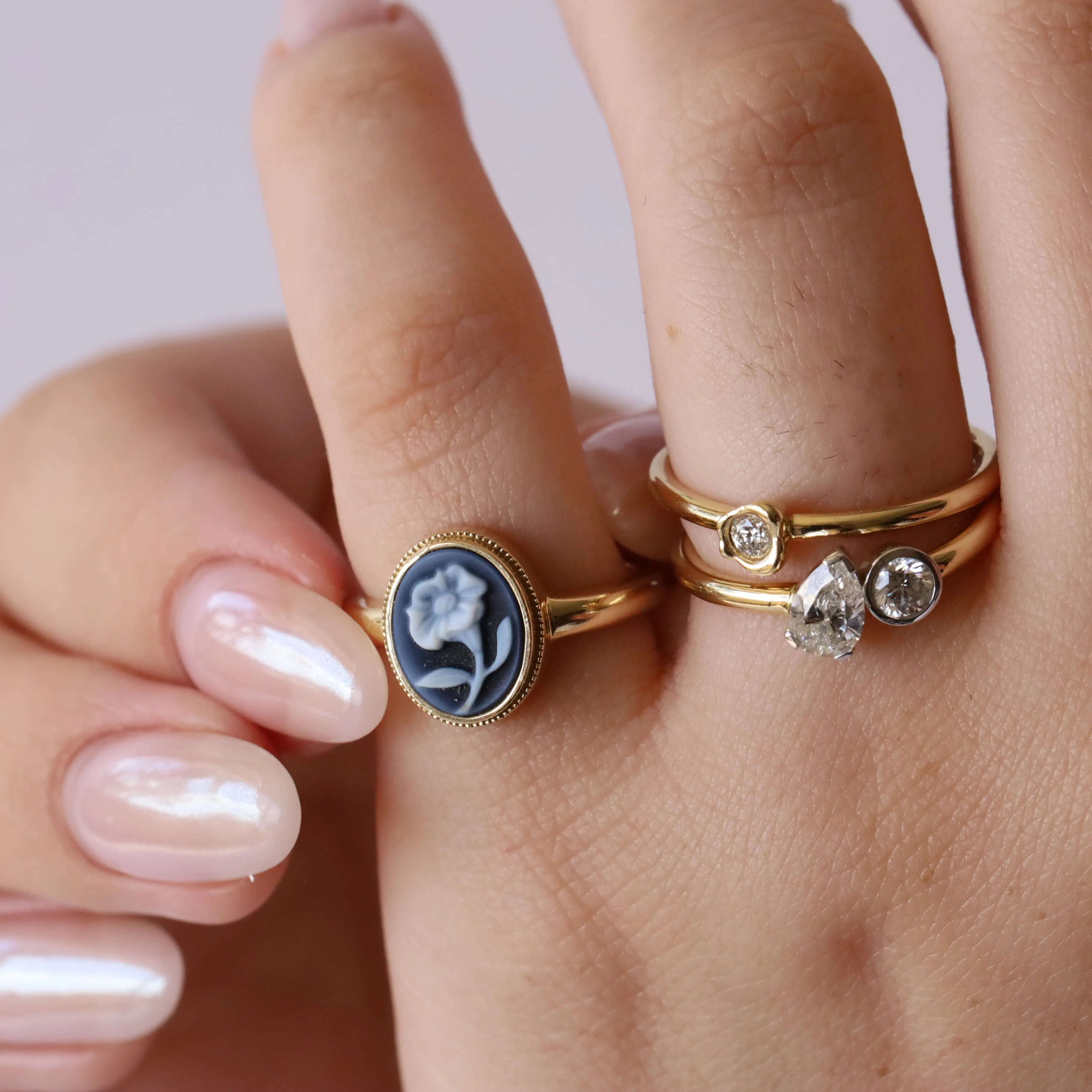 Photo of gold ring with blue flower on pinky, with two other gold diamond rings stacked on ring finger.