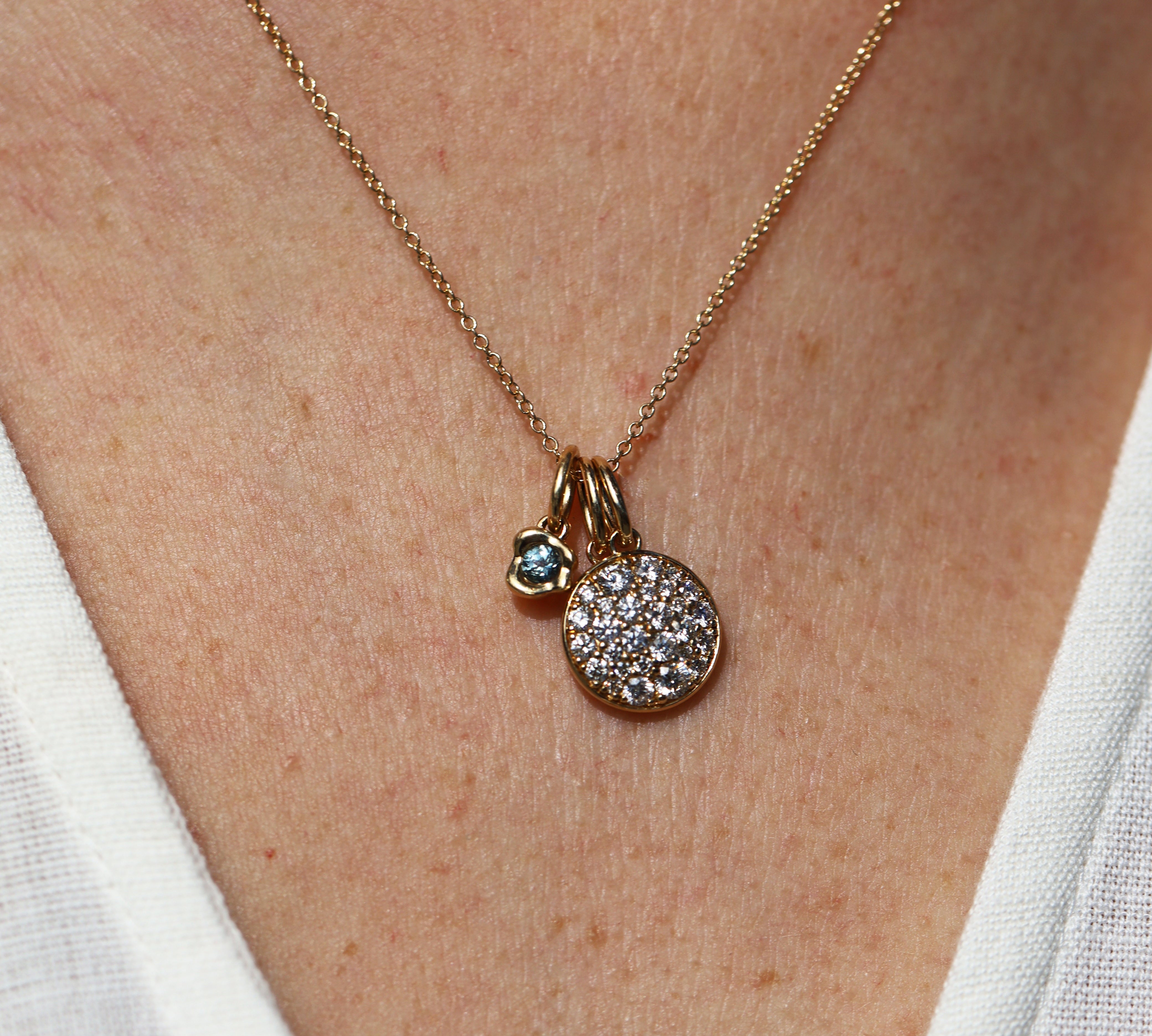 Gold necklace with two pendants on a person wearing a white top.