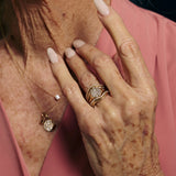 Close-up of a hand wearing a gold ring with a pink background