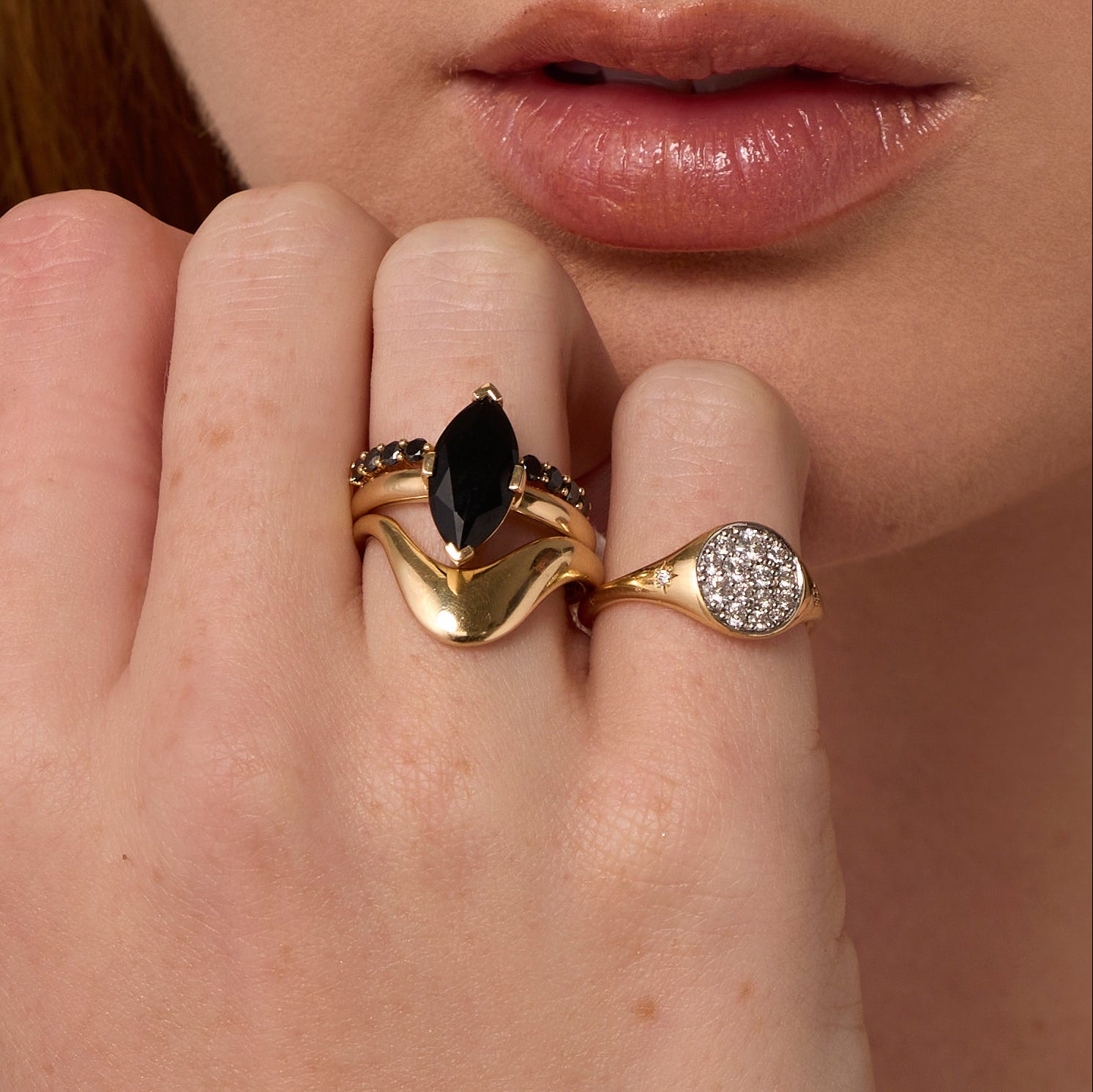 Close up of woman resting hand against her chin, highlighting multiple Marrow Fine rings styled and stacked together