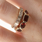 mixed shape garnet bezel band on woman's finger stacked with a diamond ring, , against a neutral background 