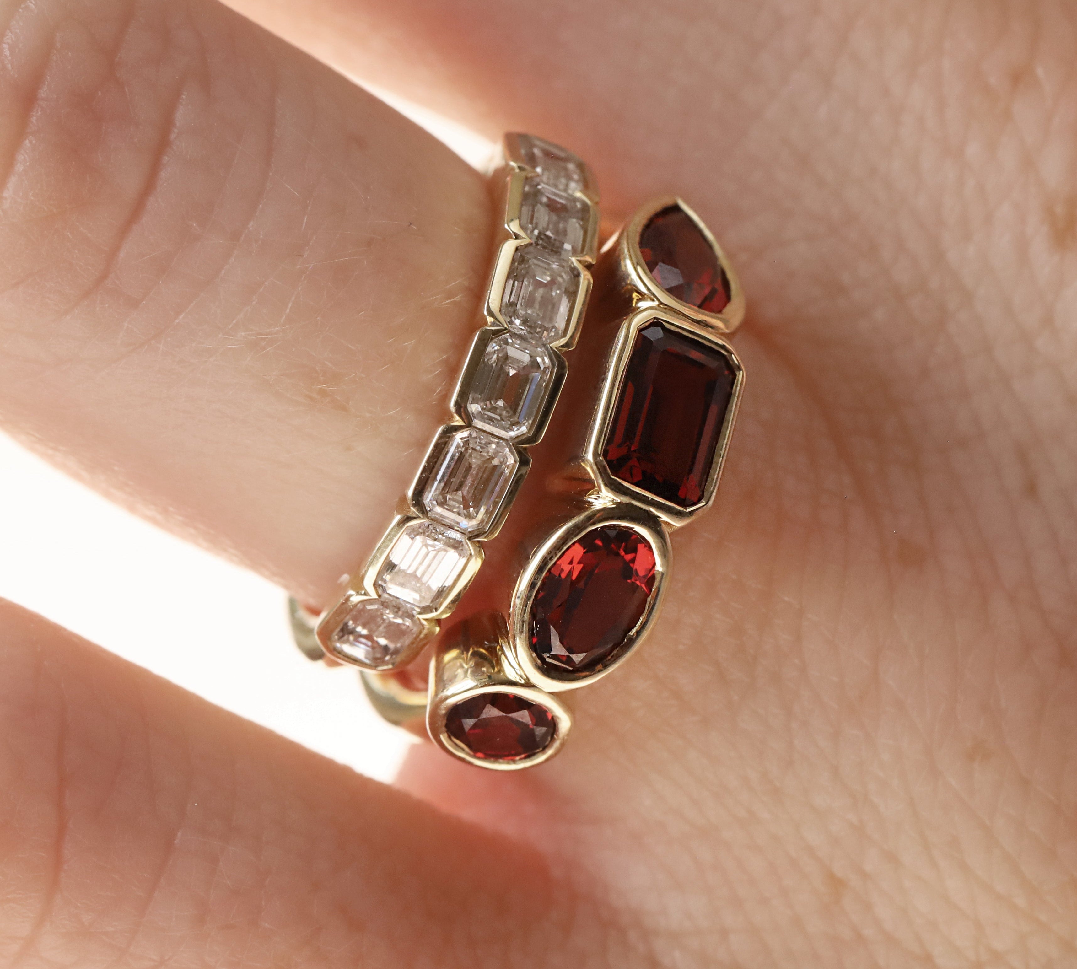 mixed shape garnet bezel band on woman's finger stacked with a diamond ring, , against a neutral background 