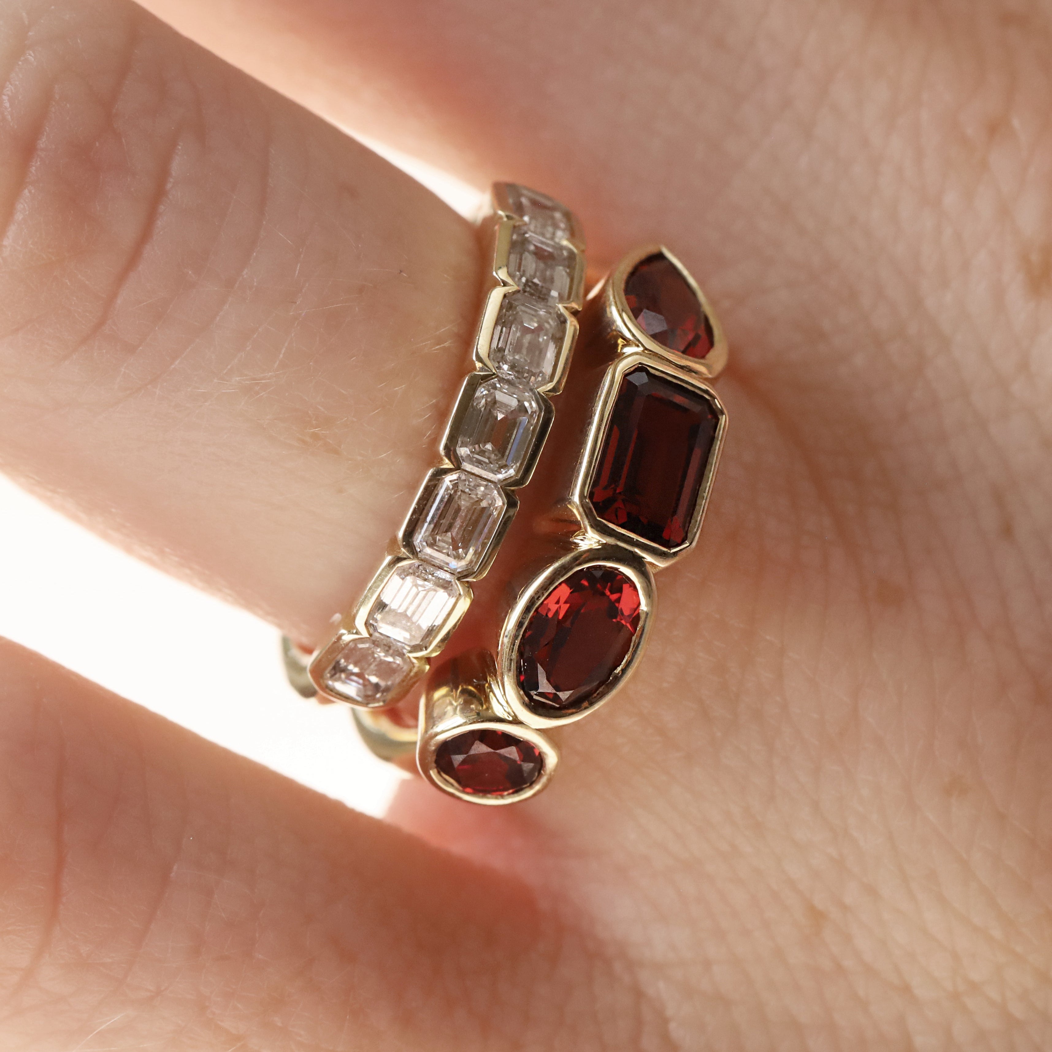 mixed shape garnet bezel band on woman's finger stacked with a diamond ring, , against a neutral background 