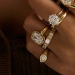 A close-up lifestyle shot of a woman wearing multiple gold rings with clear gemstones, a matching gold earring, and a brown ribbed knit top.