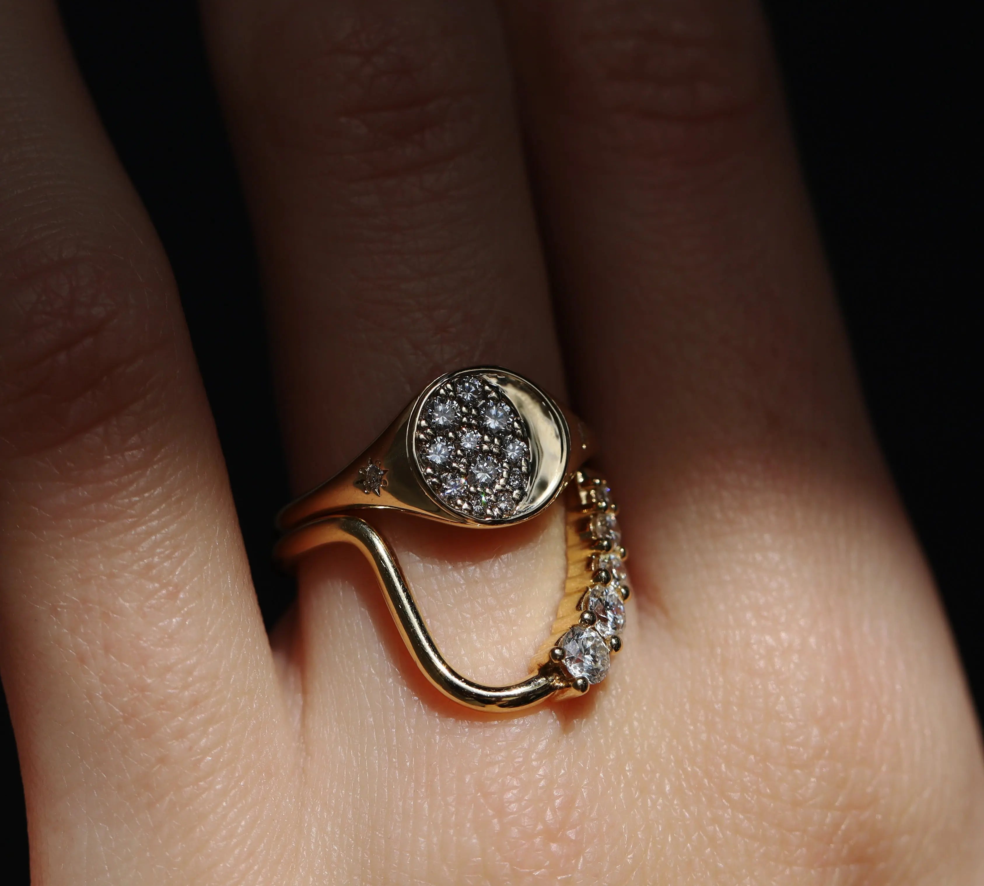 Gold ring with diamond accents on a finger against a dark background