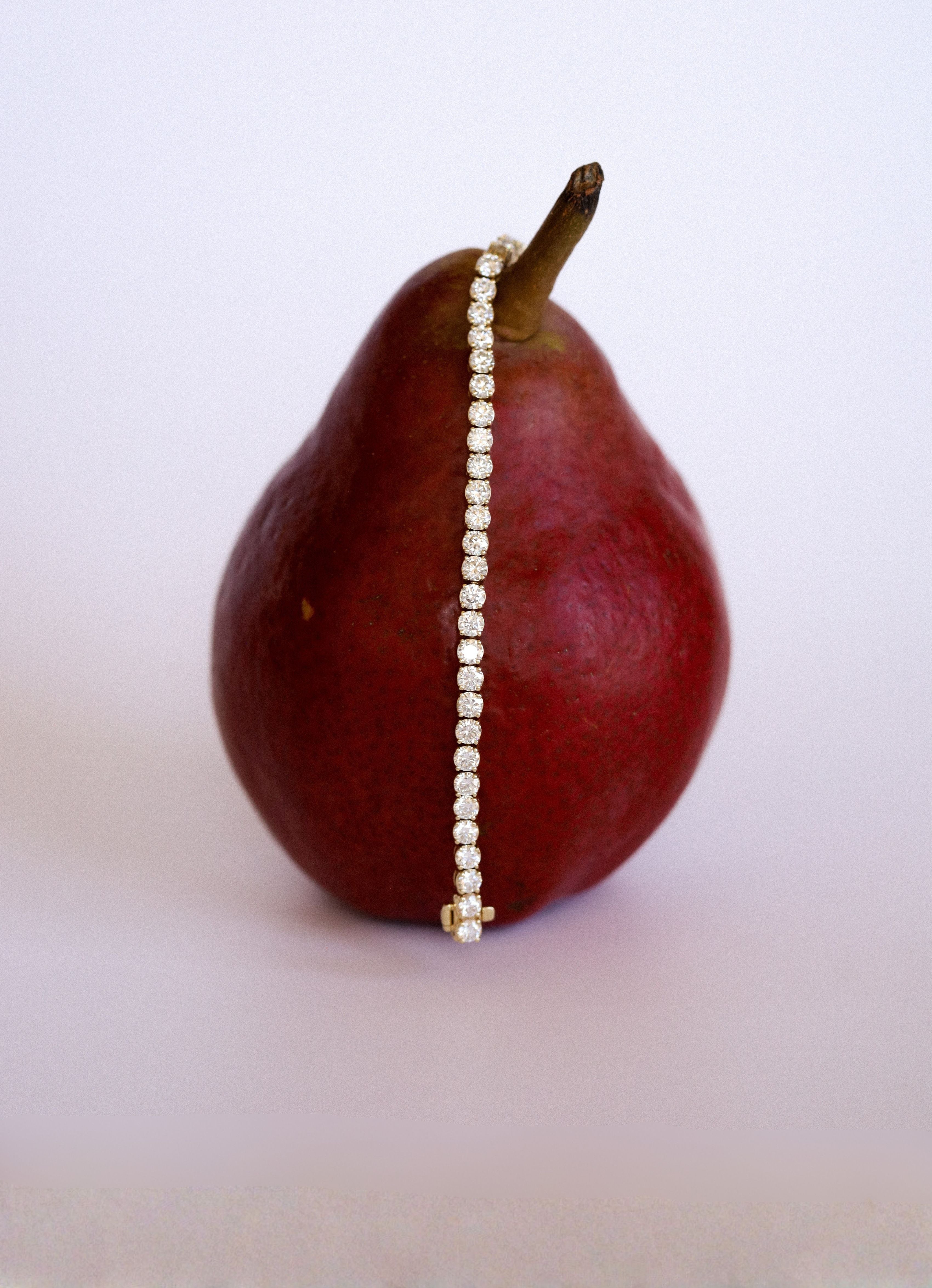 Pear with a diamond tennis bracelet draped over it on a white/neutral background