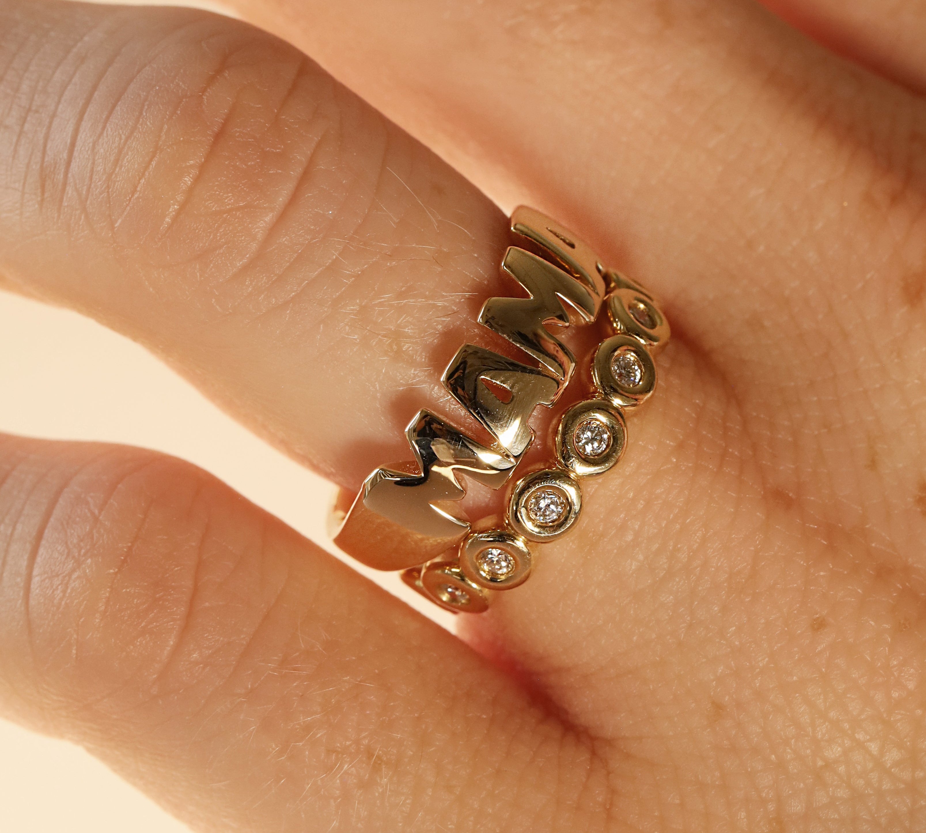 close up of woman's hand with gold MAMA ring and another yellow gold and diamond band
