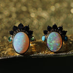 Pair of opal earrings with black and green gemstones on a reflective surface.