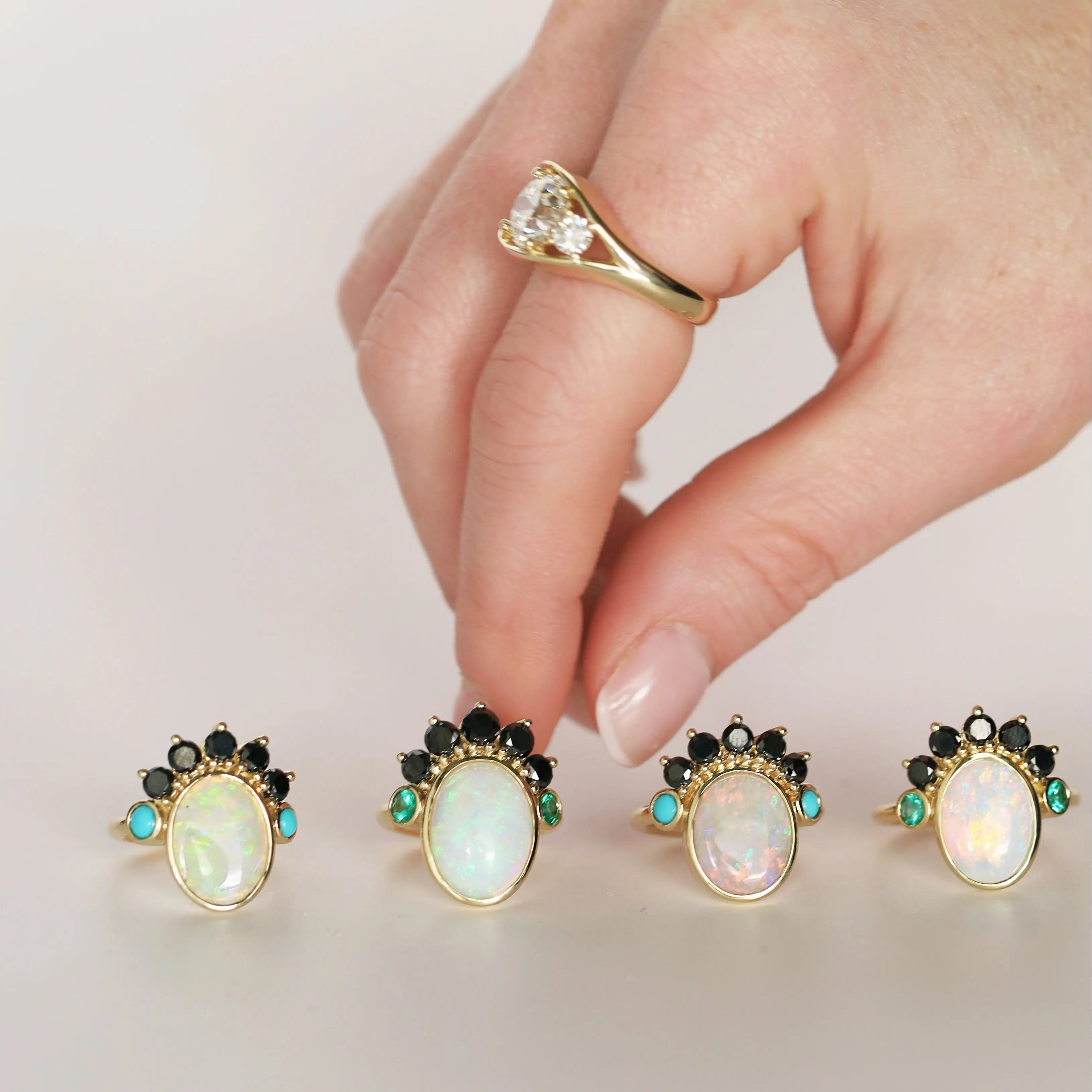 four opal rings with black diamond headdress on a white surface, and a hand reaching for one
