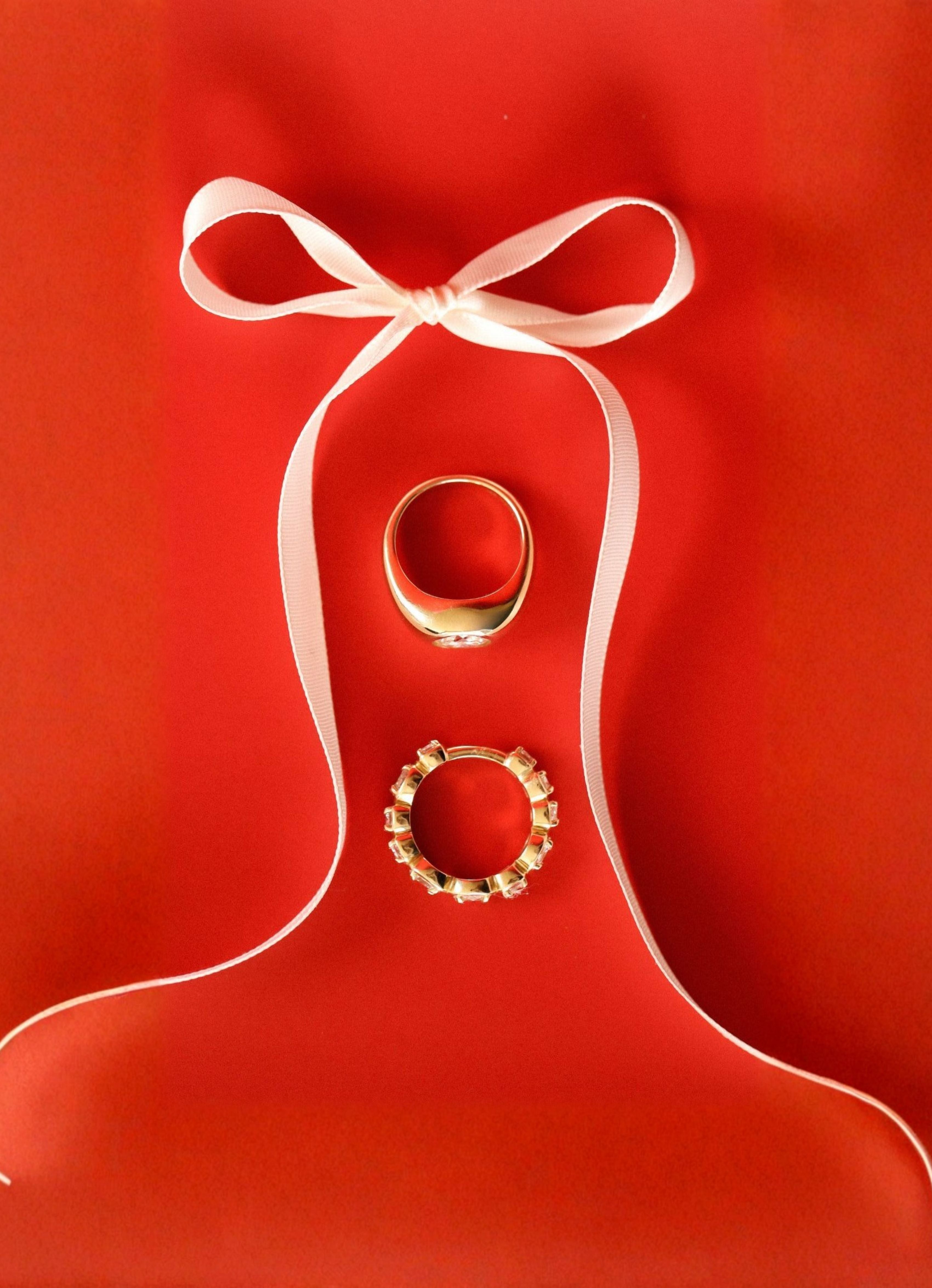Two gold rings on a red background with a white ribbon
