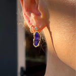 Close-up of a person wearing a gold earring with a boulder opal gemstone.