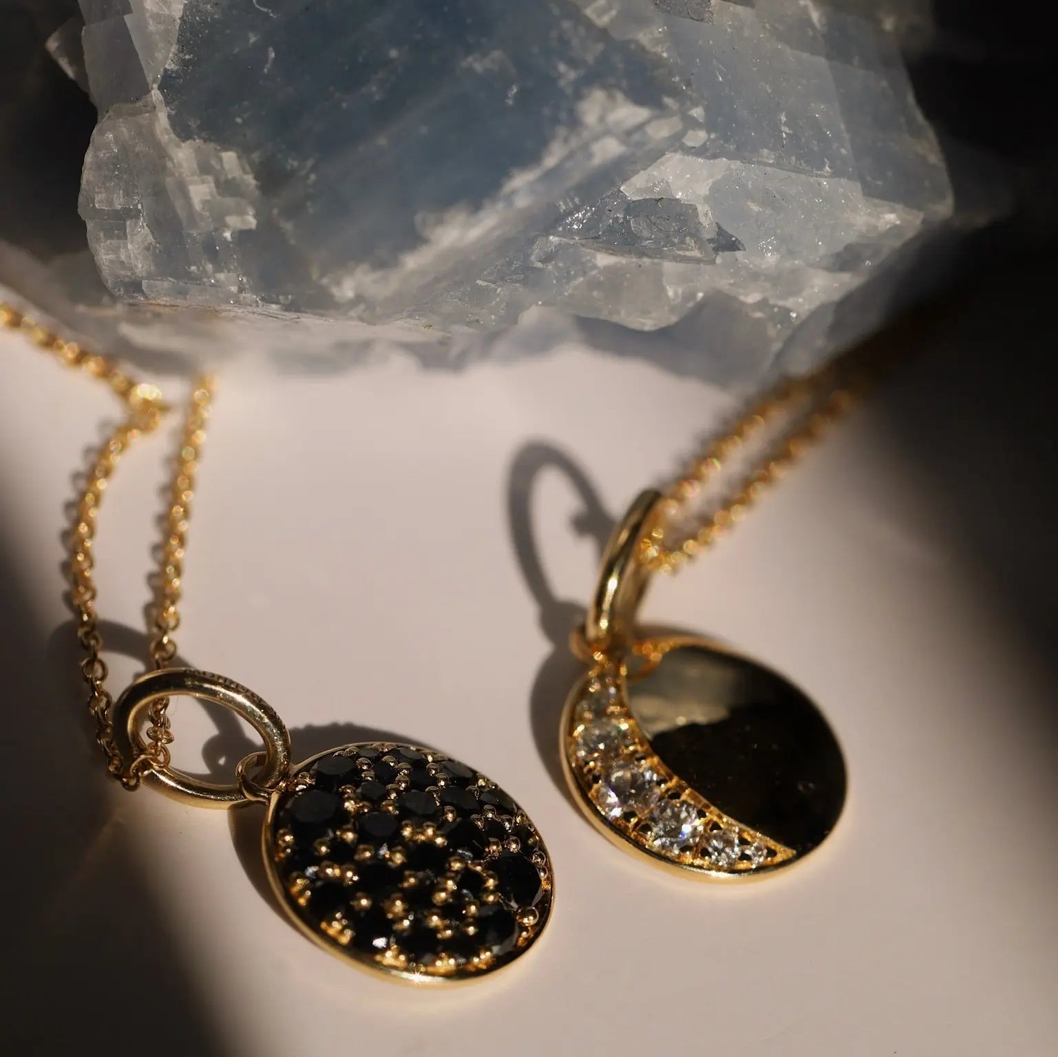 Gold necklaces with black and diamond pendants on a light background