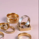 A set of six rings in various styles and metals, including yellow gold, silver, and a two-tone gold and silver band, arranged on a soft pink background.