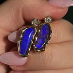 Close up of hand holding pair of boulder opal earrings