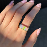 Hand wearing a ring with an opal gemstone against a dark background