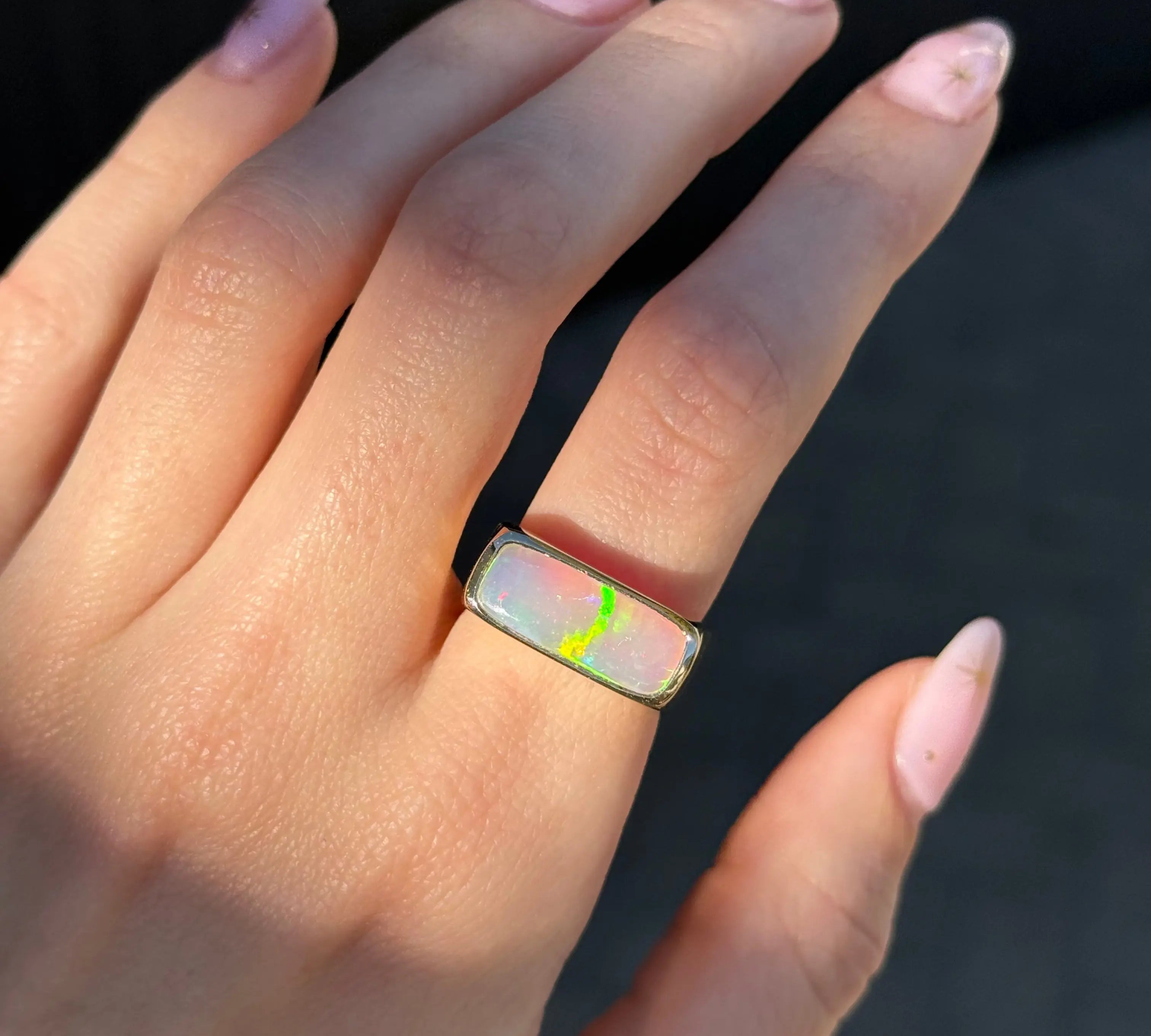 Hand wearing a ring with an opal gemstone against a dark background