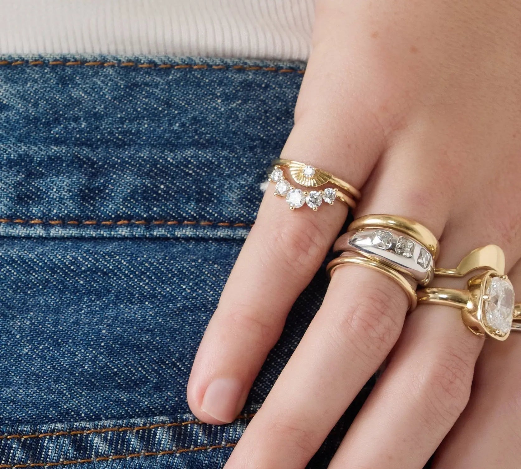 Hand wearing multiple gold rings with gemstones against a denim background