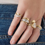Hand wearing multiple gold rings with gemstones against a denim background