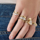 Hand wearing multiple gold rings with gemstones against a denim background