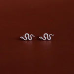 Pair of white gold snake-shaped earrings on a dark red background