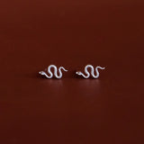 Pair of white gold snake-shaped earrings on a dark red background