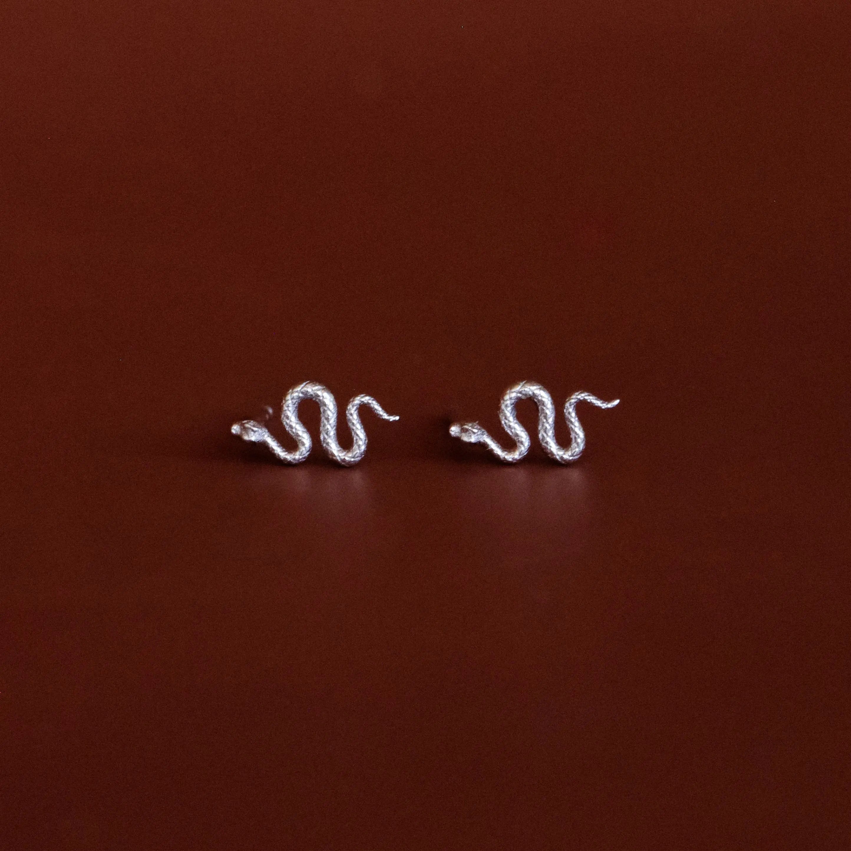 Pair of white gold snake-shaped earrings on a dark red background