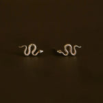 pair of gold snake earrings on a brownish green background