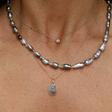 Close-up of layered necklaces with pearls and gemstones on a person's neck.