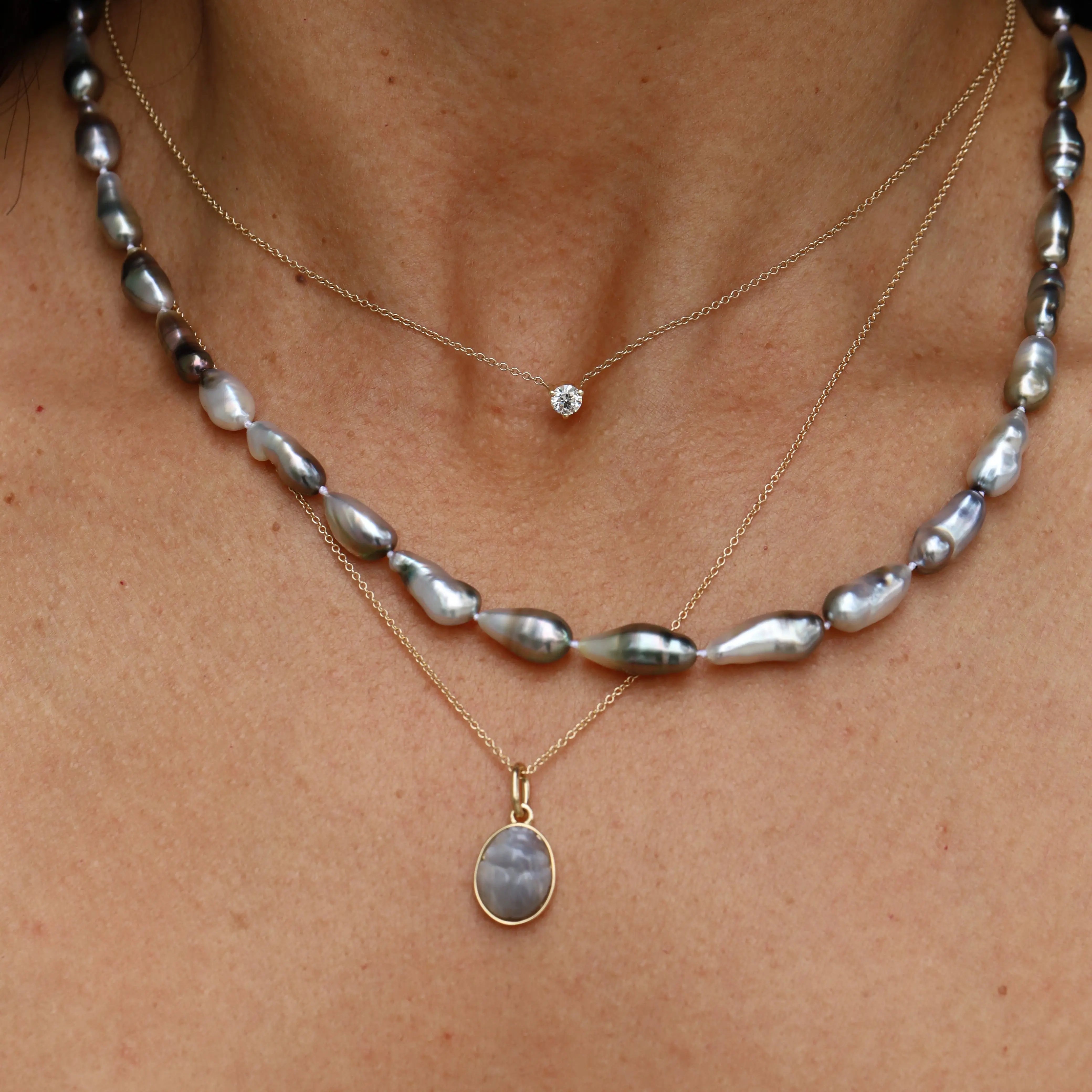 Close-up of layered necklaces with pearls and gemstones on a person's neck.