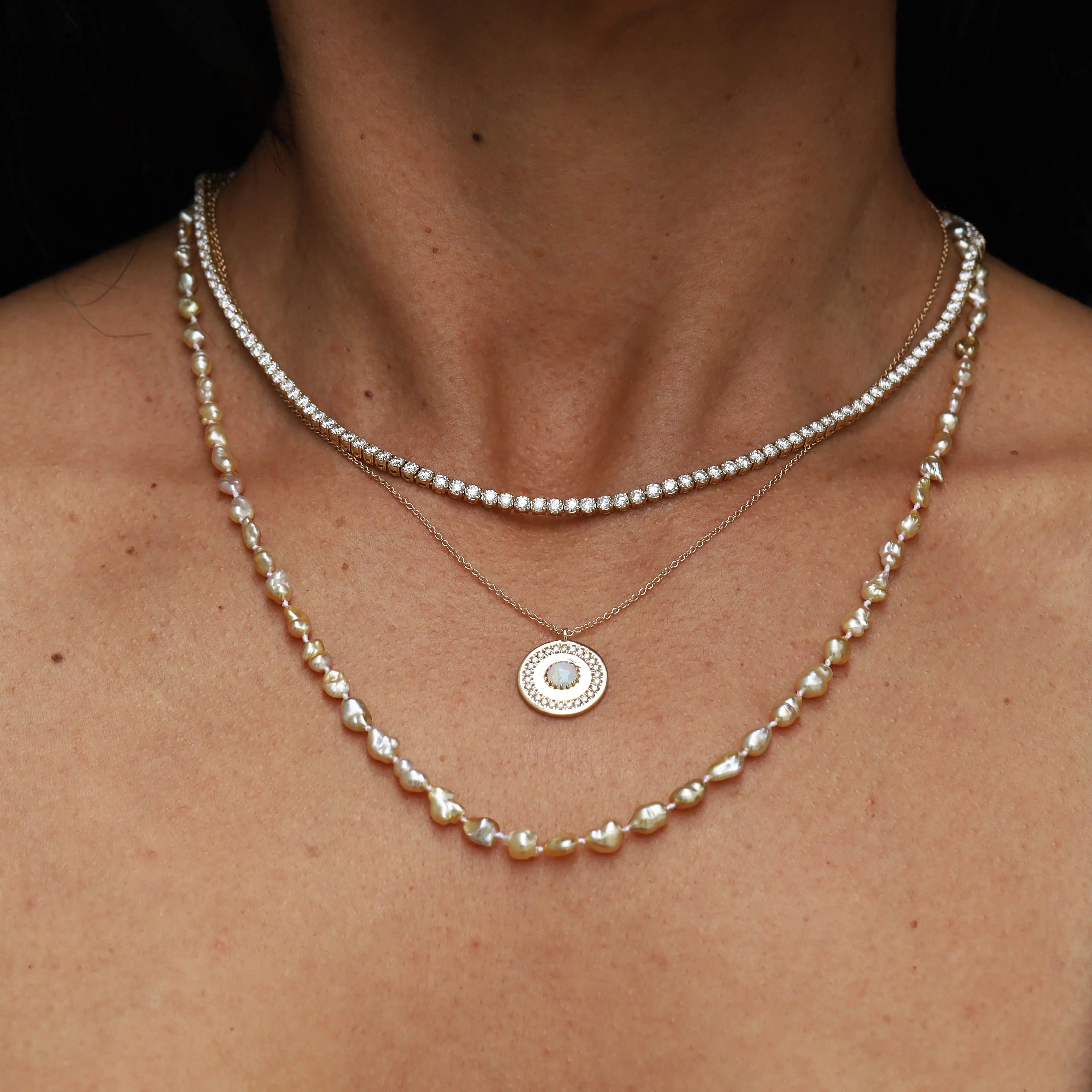 Close-up of a person wearing multiple pearl necklaces against a black background