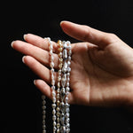 Hand holding three pearl necklaces against a black background