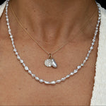 Pearl necklace with a gold chain and heart-shaped pendant worn by a person.