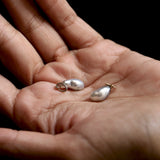 Two pearl-shaped jewelry charms on a person's palm against a dark background