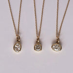 Three gold necklaces with diamond pendants on a light gray background